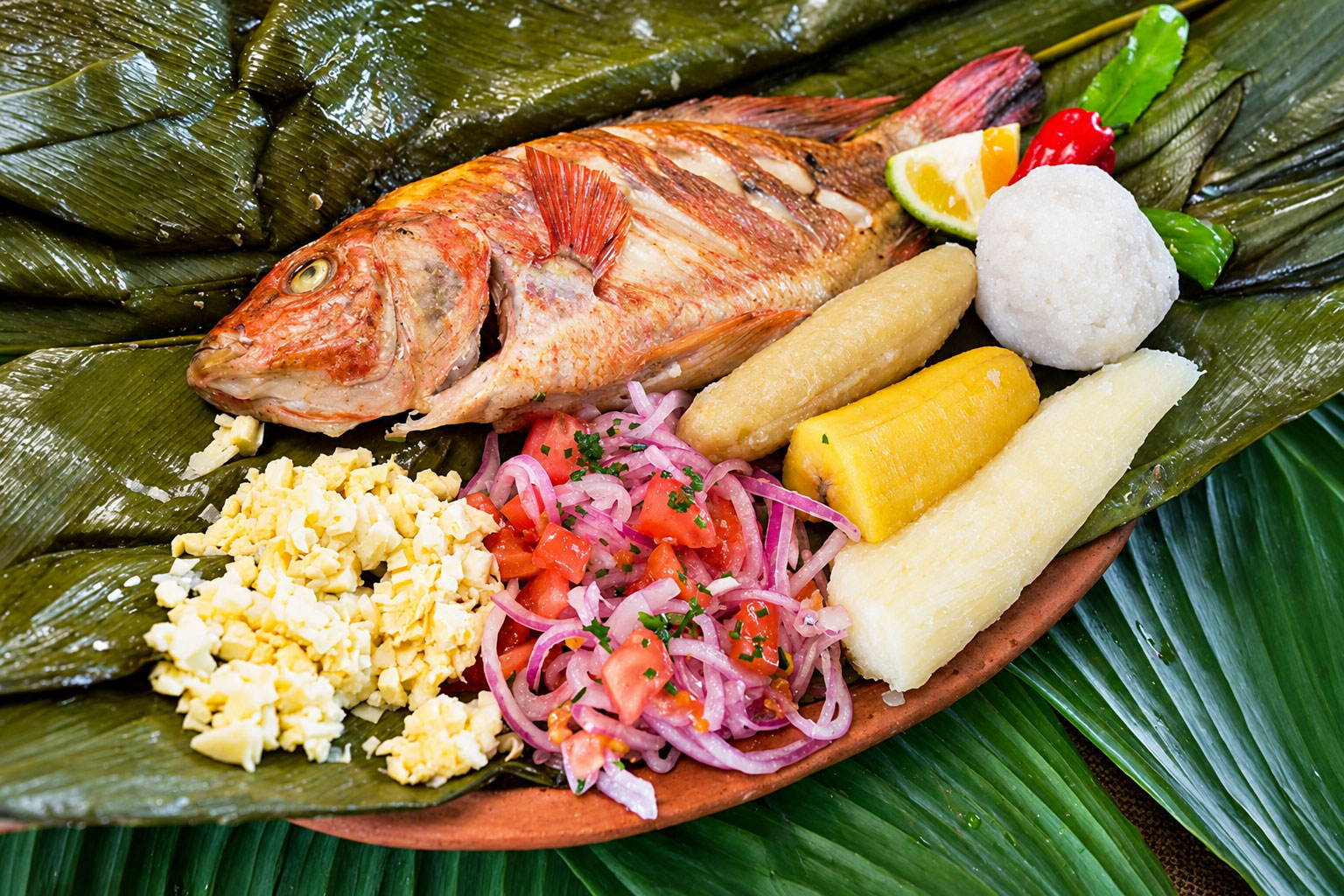 Maito de pescado y acompañamientos servido sobre hojas de bijao